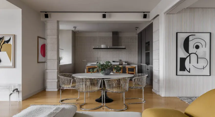 Nowoczesne wnętrze z okrągłym stołem i krzesłami w stylu bauhaus. W tle kuchnia i abstrakcyjne obrazy.