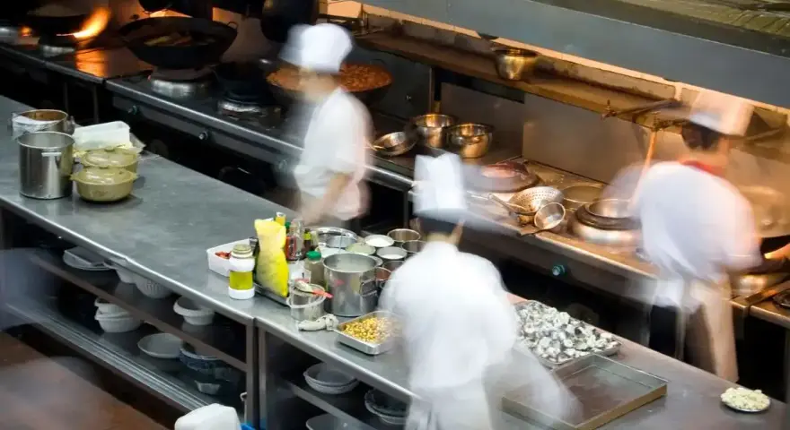 Chefs en movimiento en una cocina profesional, con ollas humeantes y ingredientes listos. El "mise en place" es clave para la eficiencia.