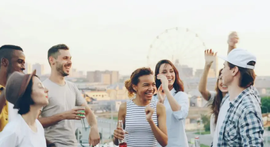 Un groupe d'amis souriants et dansant sur un toit, avec une grande roue en arrière-plan.