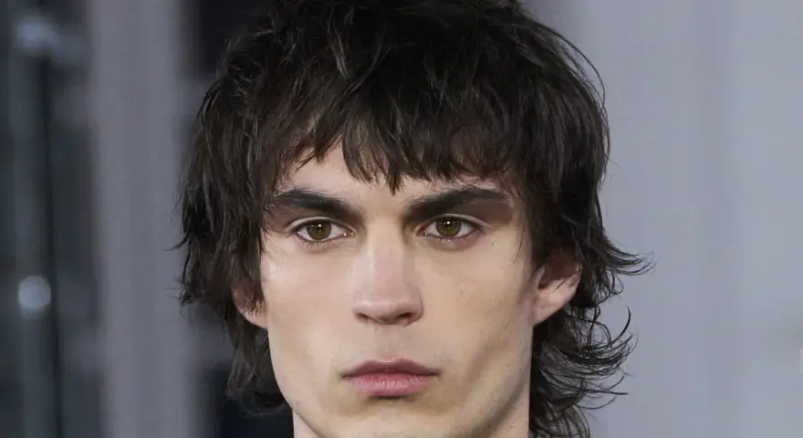 Joven con un corte de pelo mullet desordenado, mirada intensa y cejas marcadas.