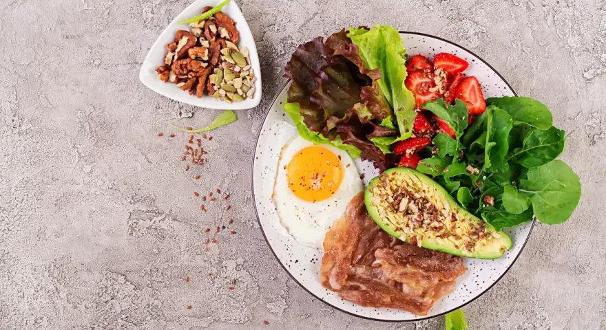 Śniadanie LCHF: jajko sadzone, boczek, awokado, sałatka z truskawkami i orzechy. Idealne na początek dnia, gdy zastanawiasz się lchf co to.