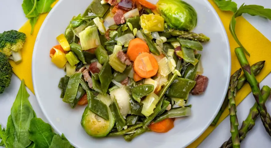 Menestra de verduras variadas con trozos de jamón en un plato blanco.