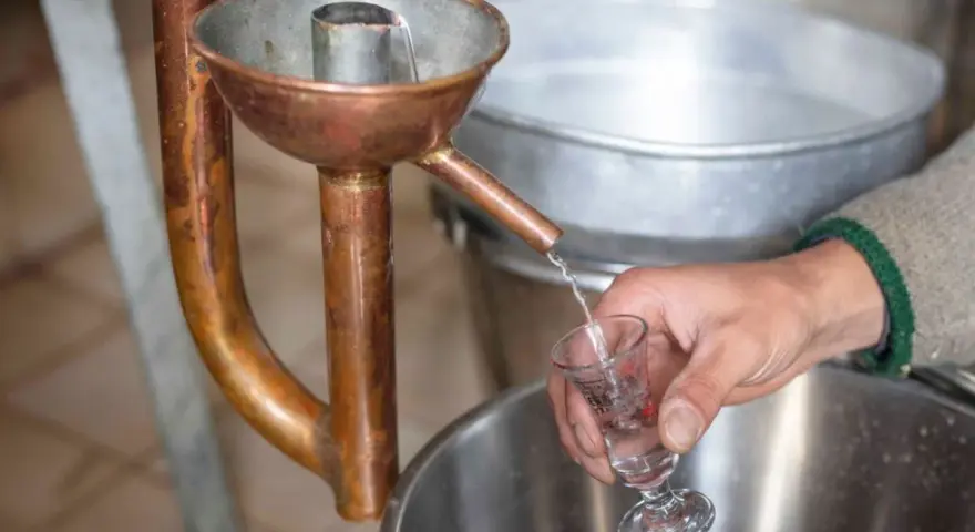 Ein Schnaps wird in ein Glas destilliert. Die Kupferapparatur zeigt, wie man Schnaps brennt.