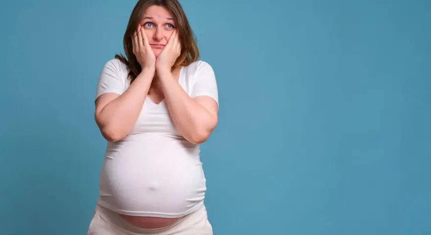 Donna incinta con le mani sul viso esprime paura in gravidanza, preoccupata per il futuro.
