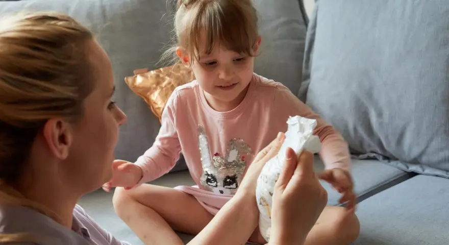 Mama pokazuje córce pieluchę, symbolizując etap, kiedy dziecko przestaje nosić pieluchy.