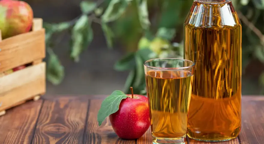 Manzana roja junto a un vaso y botella de vinagre de manzana para limpiar. Cosecha fresca en caja de madera al fondo.