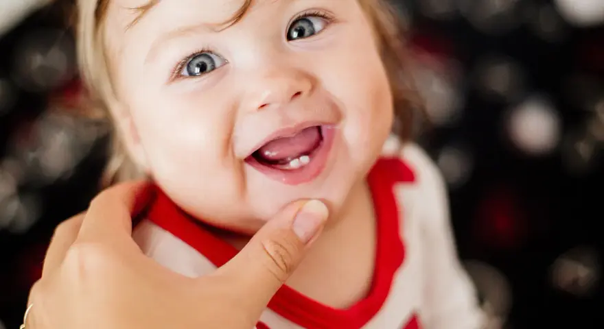 Ein lächelndes Baby mit blauen Augen zeigt stolz seine ersten Zähnchen. Das Baby zahnen ist ein aufregender Meilenstein!