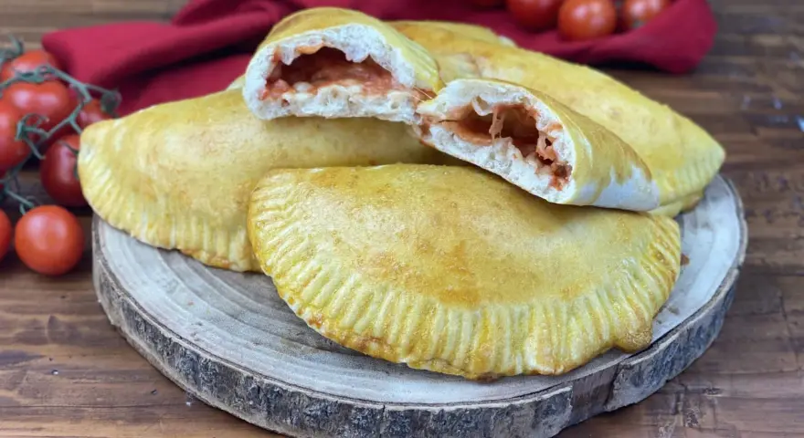 Panzerotti al forno dorati e ripieni di pomodoro e mozzarella filante, pronti per essere gustati.