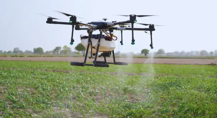A drone sprayer, one of the types of drones in agriculture, hovers over a field, dispensing liquid onto crops.