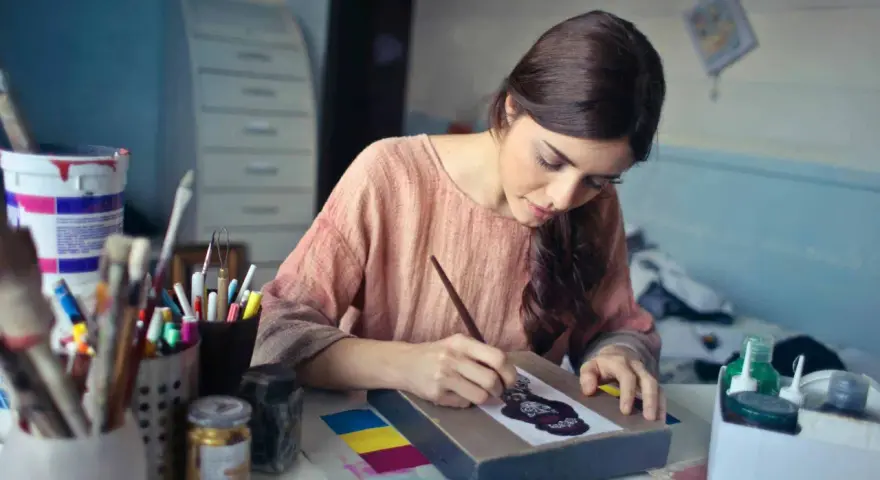 Une jeune femme se déclare artiste libre, concentrée sur sa toile, entourée de pinceaux et de peintures.