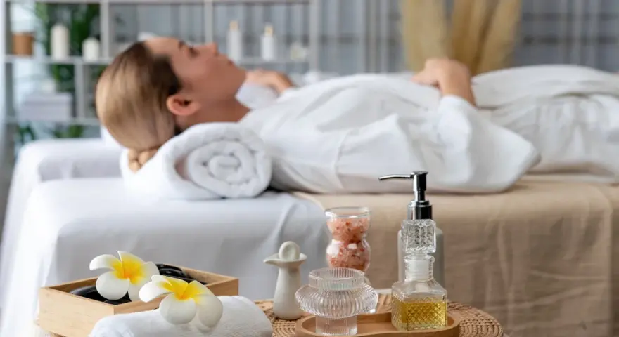 Relaks w jednym z hoteli spa Polska. Kobieta w białym szlafroku leży na łóżku, otoczona kosmetykami i kwiatami.