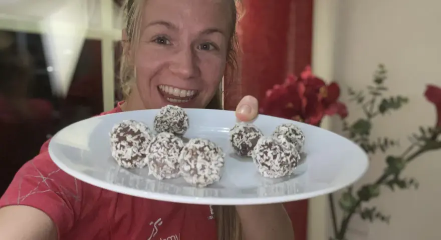 Glad kvinna visar upp en tallrik med hemgjorda chokladbollar, perfekta för ett snabbt och enkelt chokladbollar recept.