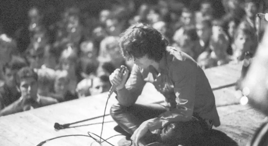 Jim Morrison z The Doors na scenie, wpatrzony w tłum. Jego "Paris Blues" rozbrzmiewa w sercach fanów.