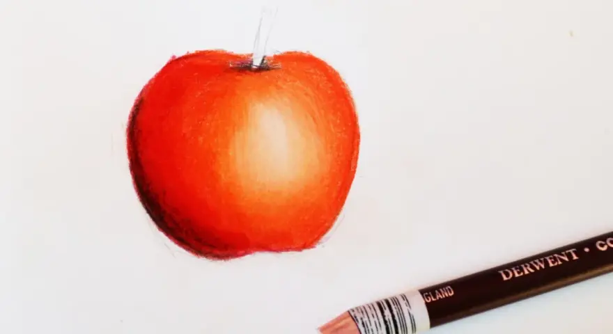 Czerwone jabłko z subtelnymi przejściami tonalnymi, pokazujące, jak cieniować kredkami. Obok leży kredka Derwent.