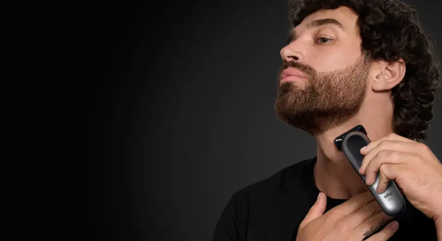 Hombre con barba cola de pato, perfil, usando una recortadora Braun para definir su estilo.