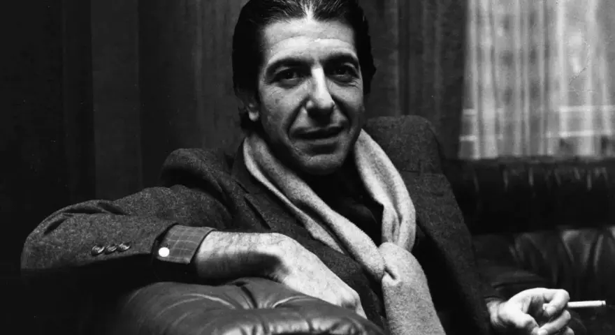 Leonard Cohen, mit Schal und Zigarette, sitzt nachdenklich auf einem Ledersofa. Ein ikonisches Bild, das den Geist des Sängers einfängt.