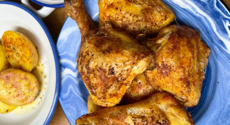 Pollo dorado y jugoso troceado en un plato azul, acompañado de patatas y pimientos.