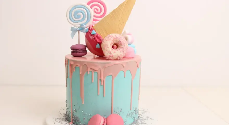 Bunter Drip Cake mit rosa Glasur, Lollis, Macarons und einem Eiswaffel-Horn.