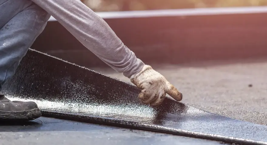 Hand mit Handschuh legt neue Dachpappe an. Alte Dachpappe entsorgen ist der nächste Schritt.