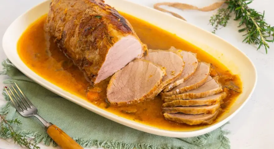 Redondo de ternera jugoso en salsa, cortado en rodajas, servido en plato ovalado blanco.