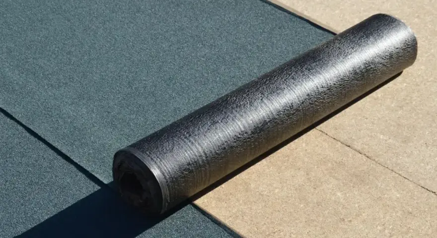 Rolka papy z połyskującą folią aluminiową leży na ciemnozielonej powierzchni.