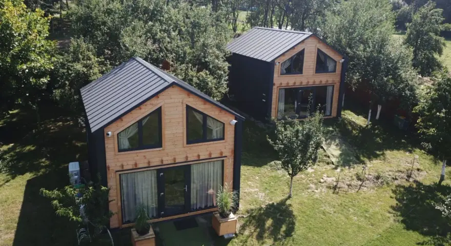 Dwa nowoczesne domki z drewna i czarnego panelu, idealne projekty domów pod wynajem, otoczone zielenią.