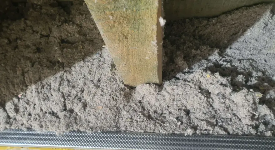 Izolacja z celulozy wypełnia przestrzeń między drewnianymi belkami stropowymi, tworząc warstwę termoizolacyjną.