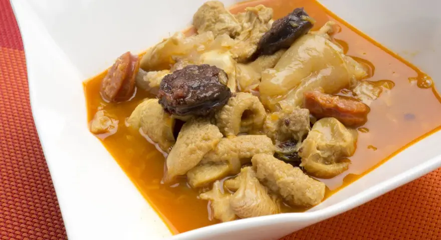 Un plato de callos a la madrileña con chorizo y morcilla en una cazuela blanca.