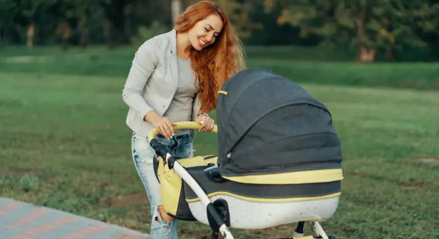 Uśmiechnięta mama z rudymi włosami pochyla się nad wózkiem. Idealny spacer, gdy zastanawiasz się, jak ubrać niemowlę 20 stopni.