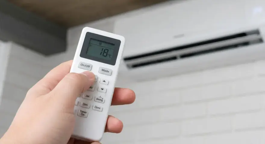 Mano ajustando el control remoto del aire acondicionado por la noche a 18 grados.