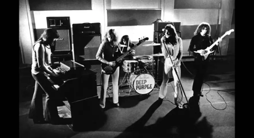 Zespół Deep Purple w akcji. Muzycy grają na instrumentach, w tle perkusja z logo zespołu.