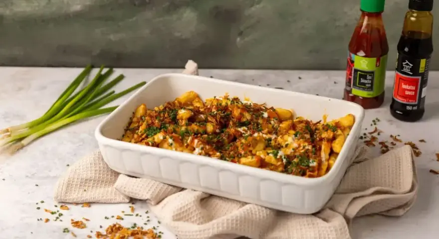 Pyszne frytki z chrupiącą posypką i sosem. Obok butelki sosu Sriracha i Tonkatsu, idealne do frytek.