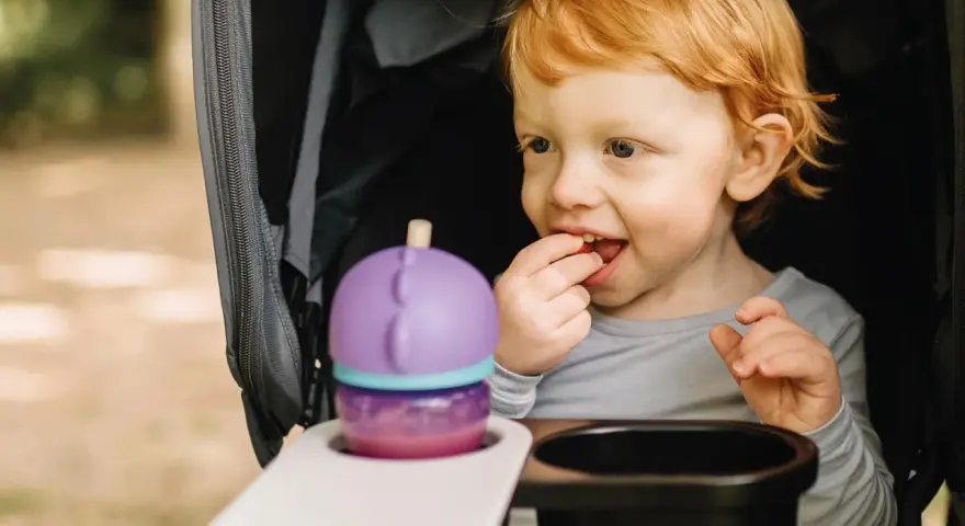 Rotschopf-Kind im Kinderwagen, isst genüsslich einen Snack. Dieses Kind hat immer Hunger und freut sich über jede Leckerei.