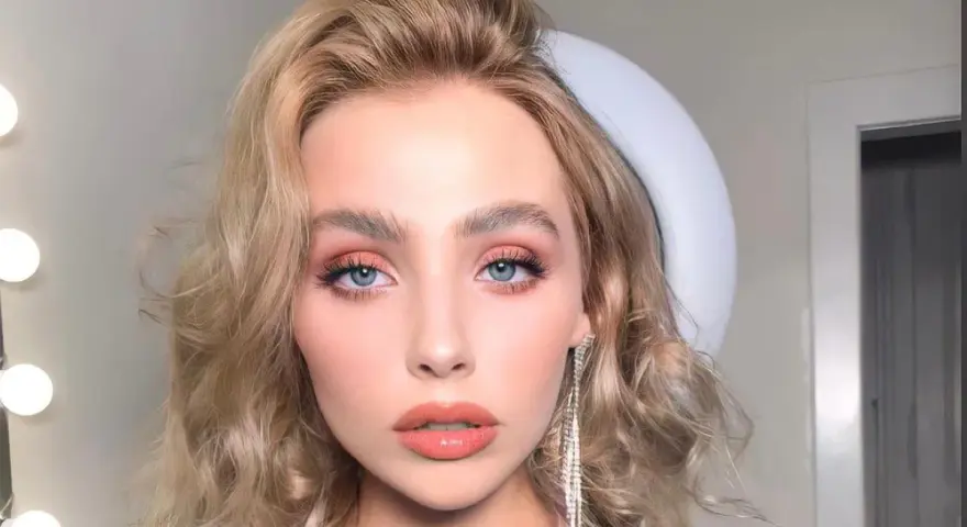 Kobieta z pięknymi, falowanymi włosami w odcieniu **naturalny średni blond**. Jej oczy podkreślone są delikatnym makijażem, a usta w kolorze brzoskwini.