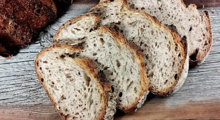 Ein Laib Sauerteigbrot, angeschnitten, mit sichtbarer, knuspriger Kruste. Die Scheiben zeigen eine luftige Krume. Hoffentlich ist die brotkruste zu hart, um sie zu genießen.