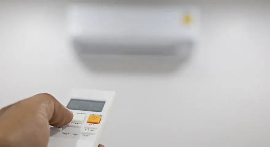 Mano che preme il telecomando per regolare il condizionatore. Il suo significato è comfort e controllo della temperatura.