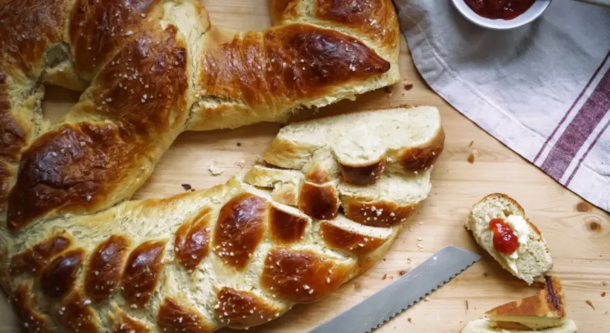 Goldbraune Neujahrsbrezel, mit Salz bestreut, auf einem Holztisch. Ein Stück ist mit Butter und Marmelade belegt. Ein tolles Neujahrsbrezel Rezept!