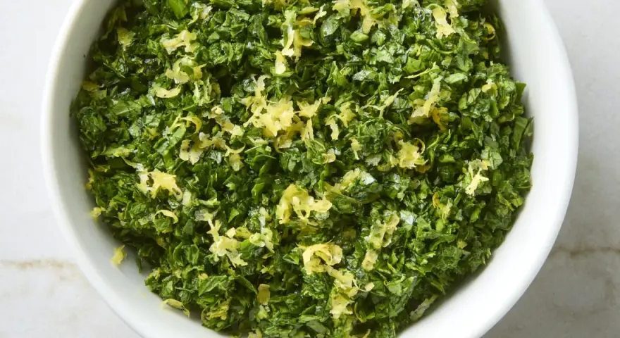 Un cuenco blanco lleno de perejil picado y ralladura de limón, perfecto para un toque fresco en tu cocina, como la albahaca en francés.