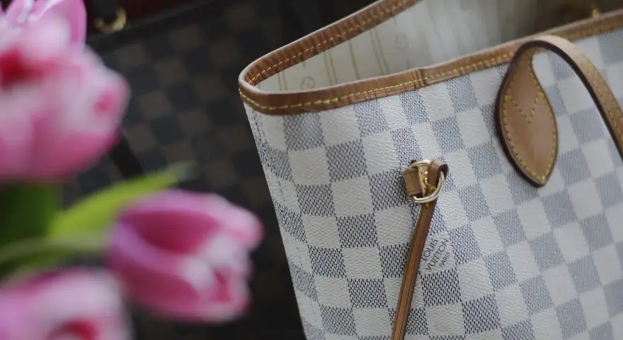 Jasna torebka Louis Vuitton w kratkę Damier Azur z różowymi tulipanami w tle.
