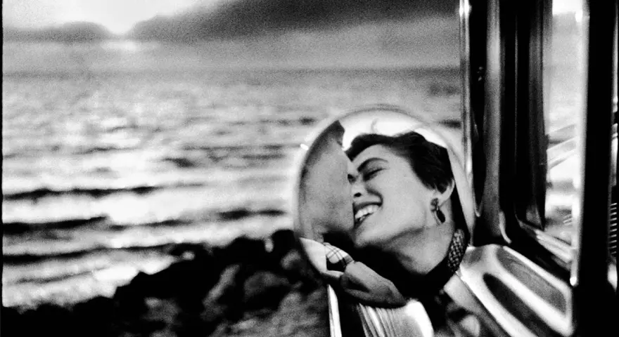 Un doux reflet dans le rétroviseur d'une voiture, une femme rit aux éclats, le regard tourné vers la mer.