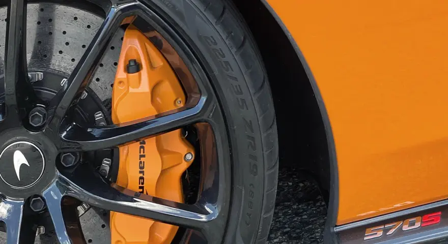 Pomarańczowy zacisk hamulcowy McLaren na czarnym, wieloramiennym kole. Opona z napisem 225/35 ZR19.
