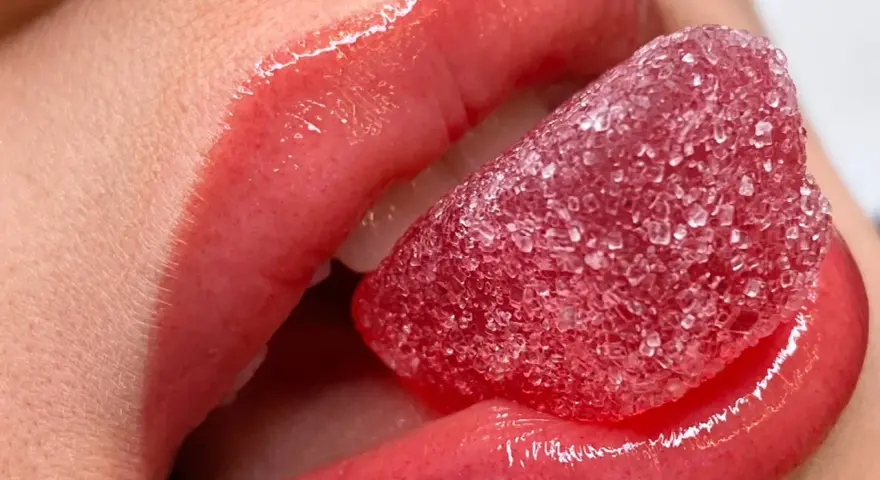Labbra carnose e lucide, con un effetto volume dato da un tatuaggio labbra, assaporano una caramella rossa zuccherina.