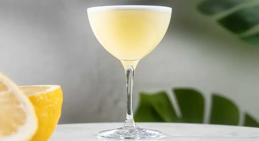 En elegant lemon martini med en lätt skumkrona, serverad med färska citronklyftor i bakgrunden.