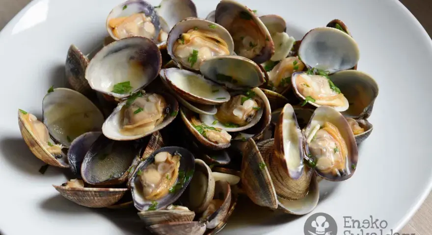 Un plato de almejas a la marinera, jugosas y recién cocinadas, con perejil picado.