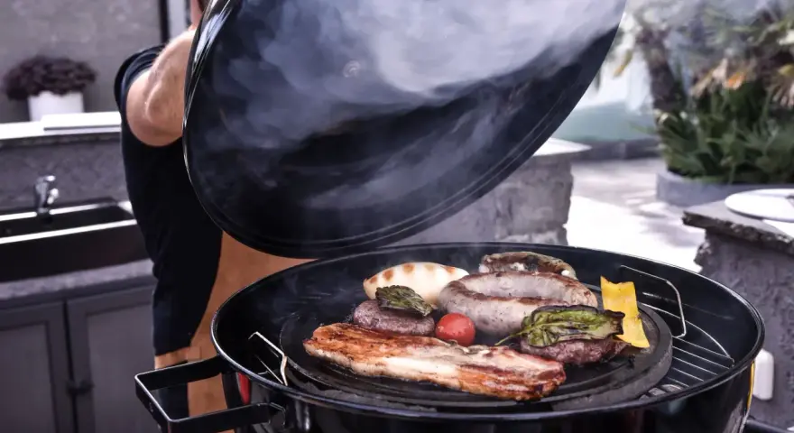 Fumo sale da una grigliata di carne succulenta, con salsicce, hamburger e pancetta che sfrigolano.