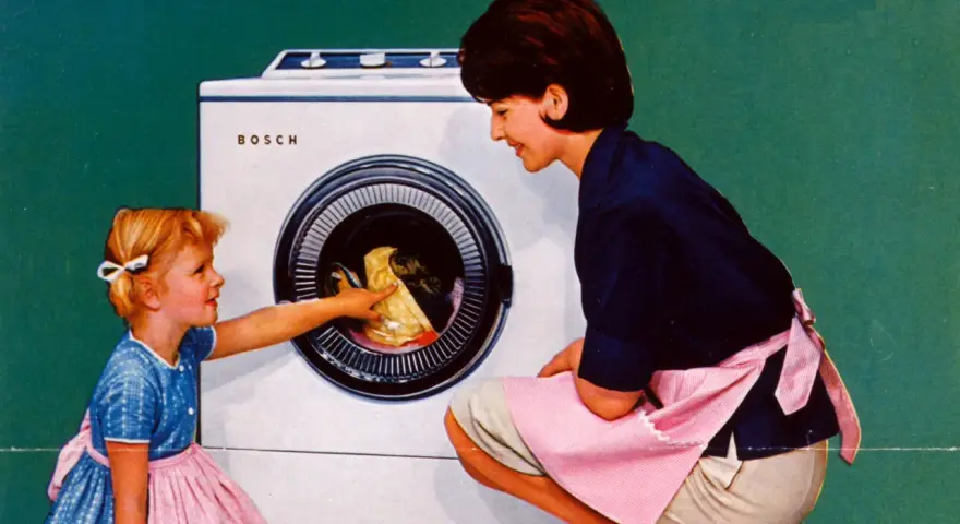 Mutter und Kind vor der ersten Waschmaschine. Das kleine Mädchen hilft beim Einräumen der Wäsche.