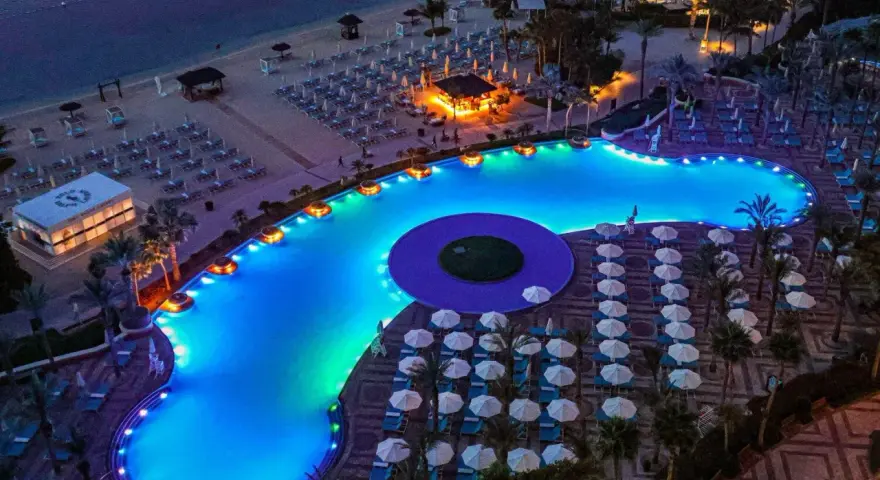 Luksusowy basen z niebieskim podświetleniem i leżakami na plaży w Dubaju.