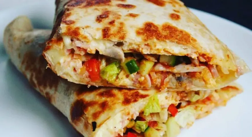 Złocista tortilla z jajkiem, serem i szynką, wypełniona warzywami, usmażona na patelni. Pyszne danie na szybki posiłek.