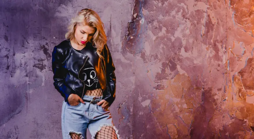 Blondynka w skórzanej kurtce i podartych dżinsach, z siatką na nogach, emanuje **grunge**'owym klimatem.