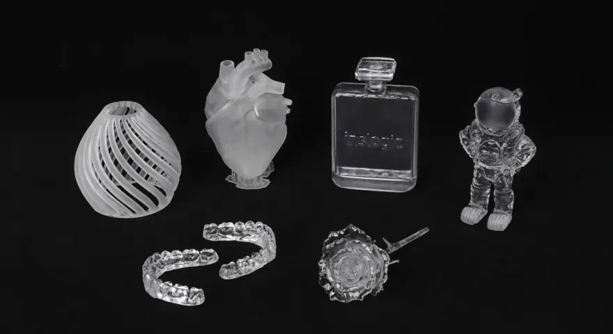 A collection of 3D printed acrylic objects: a vase, heart, dental aligners, perfume bottle, rose, and astronaut.